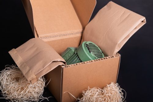 Fibre de bois naturelle en vrac et en enveloppe papier utilisée comme calage écologique dans des cartons, protégeant une pièce industrielle pendant le transport.